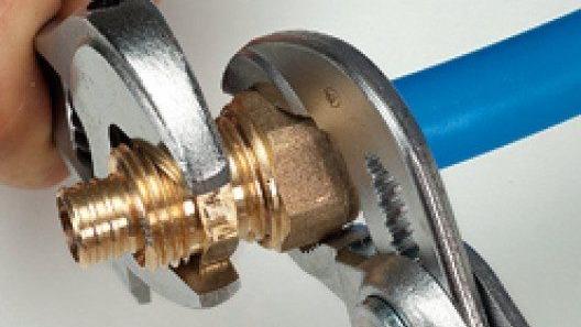 Llave inglesa apretando un racor de latón sobre tubería azul